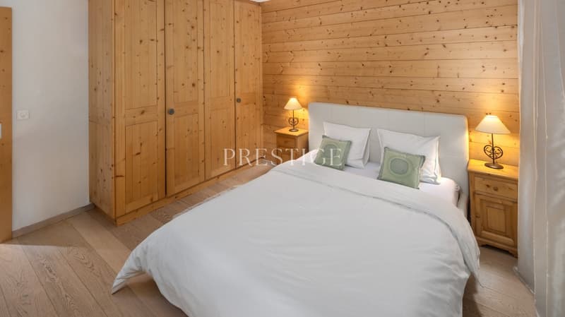 Bedroom with wooden walls, wooden floor, bed with white bedding, wooden nightstands with lamps, wooden wardrobe, white headboard