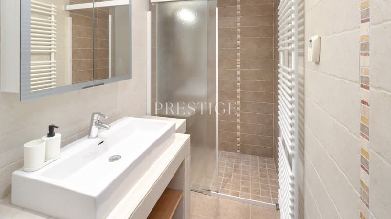 Bathroom with a white sink, mirror, glass shower enclosure, and tiled walls.