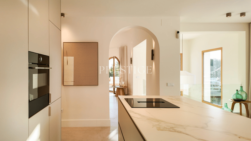 modern kitchen with marble countertop, black induction hob, built-in oven, wooden table, glass door, white walls, ceiling lights