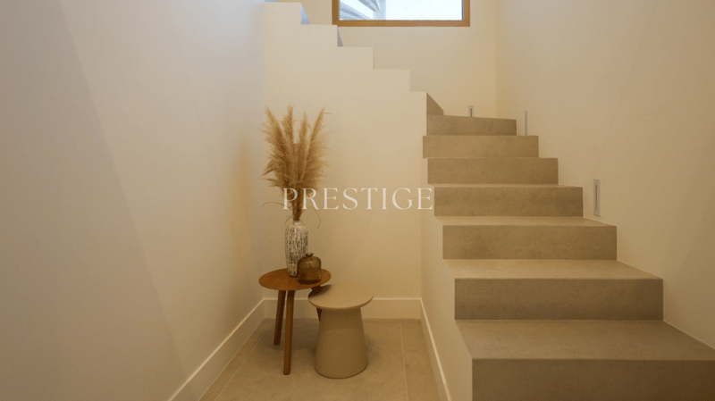 Modern staircase with beige steps, white walls, wooden table with a vase, and a stool