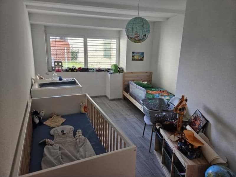 Two beds, one of which is a crib, wooden floor, sink, storage box, toys, framed pictures, lamp, children's pillow