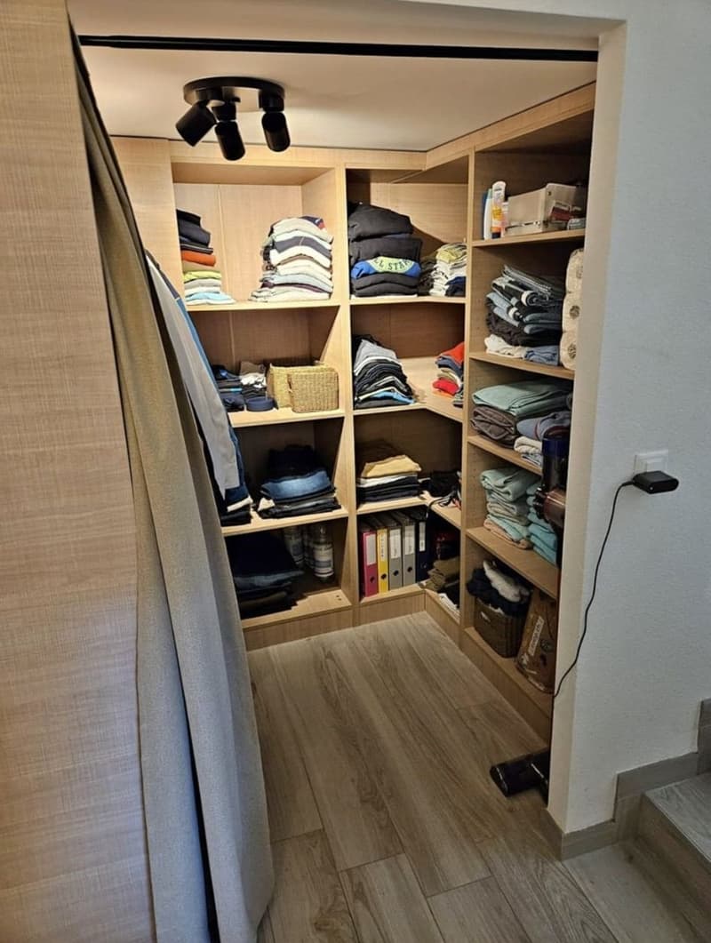 Closet with shelves, clothes on hangers, baskets, ceiling lamps, electrical outlet.