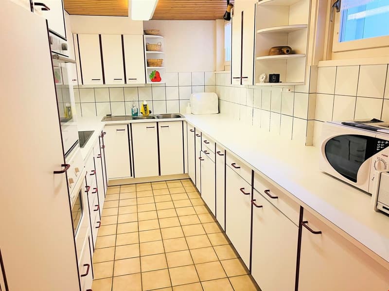 Galley-style kitchen with white cabinets, tile backsplash, tile flooring, stainless steel appliances including a dishwasher, and shelving for storage