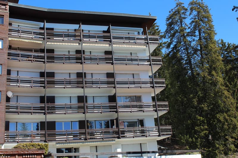 Multi-story apartment building with balconies, surrounded by trees