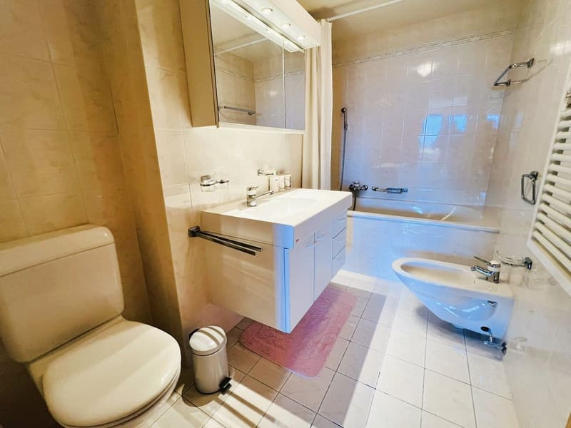 modern bathroom, white tiled floor, white bath, white sink, mirror above the sink, shower, bidet, toilet, pink towel