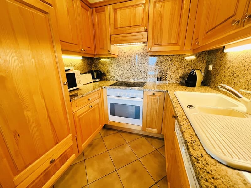 open kitchen, wooden cabinets, granite countertops, under cabinet lighting, white appliances, sink with faucet, tile flooring