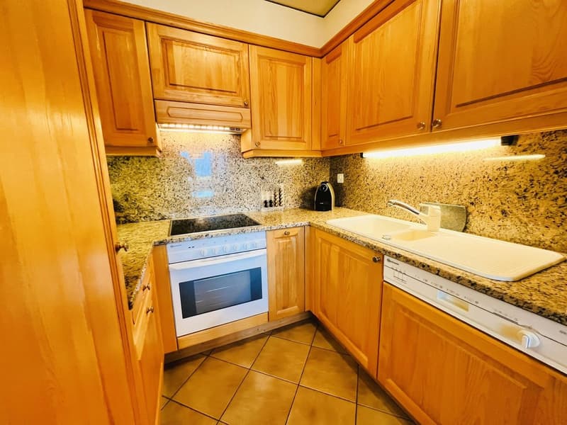 Wooden cabinets, granite countertops, white oven, black stove, sink with silver faucet, dishwasher, tiled floor, stainless steel blender on countertop.