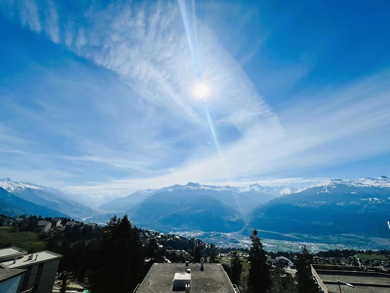 Mountain range, snow-capped peaks, vibrant blue sky, scattered clouds, trees, distant town
