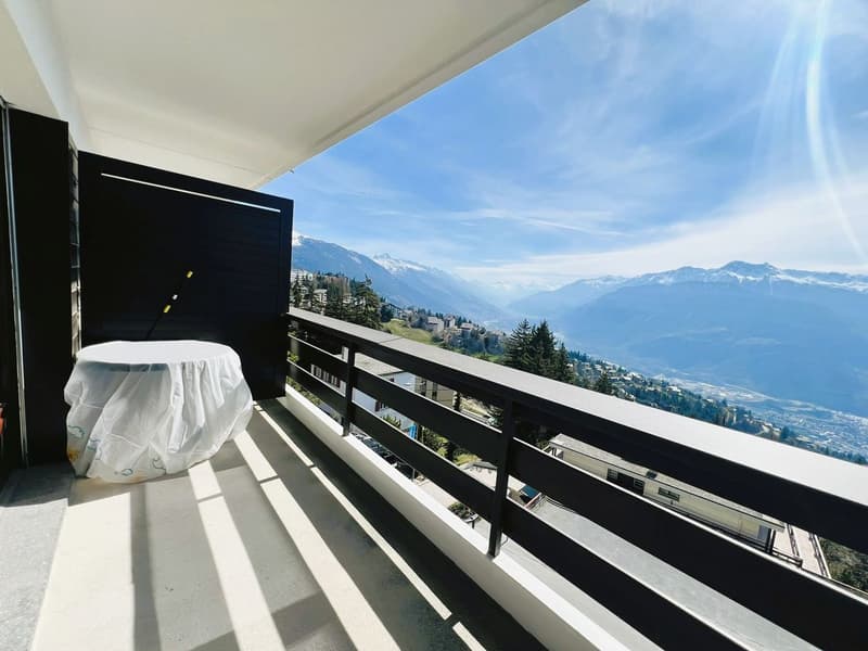 Balcony with covered table, surrounded by railings, mountainous view