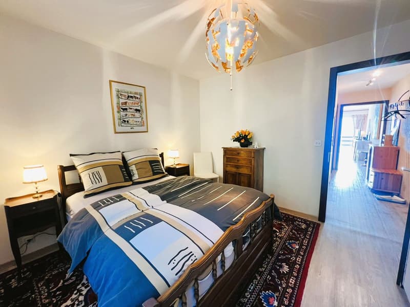 Bedroom with bed, lamps, rug, wooden furniture, picture frame, flowers, corridor