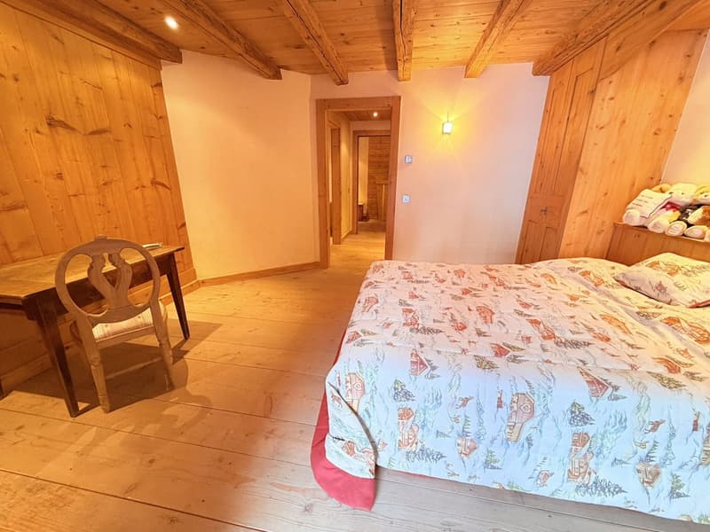 Bedroom: bed with floral bedsheet, chair, desk, wooden walls, wooden flooring.