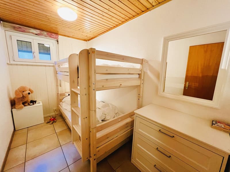 A small bedroom with a wooden bunk bed, a white cabinet, a mirror, and a stuffed toy on a white storage box.