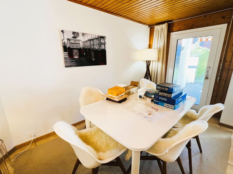 Dining room with white table, white chairs, white walls, wooden ceiling, picture frame, lamp, carpet, door, window, outdoor view