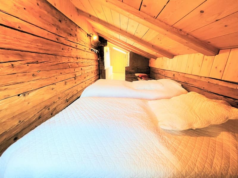 Bedroom with wooden walls, two single beds, white bedding, wooden ceiling, small lamp