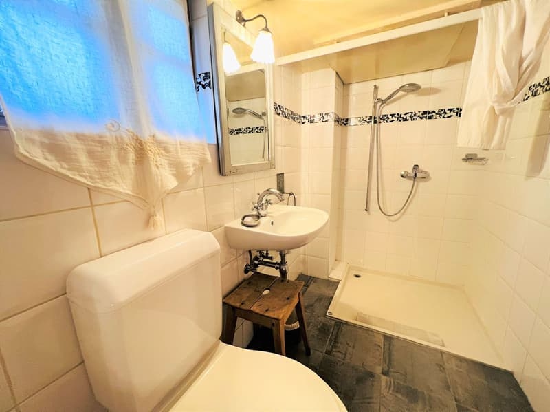 white tiles, white toilet, white sink, shower, wooden stool, mirror