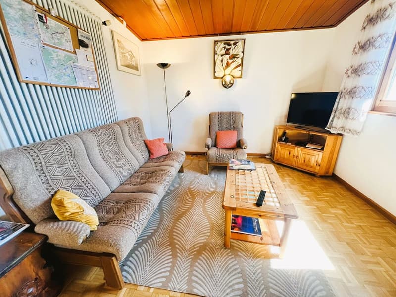 wooden floor, white walls, gray couch, wooden coffee table, TV, wooden cabinet, floor lamp, picture frames, curtains