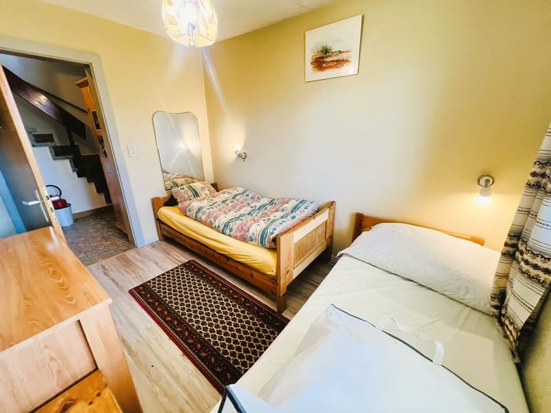 Bedroom with two single beds, wooden floor, wooden cabinet, mirror, rug, wall painting, and wall lamps