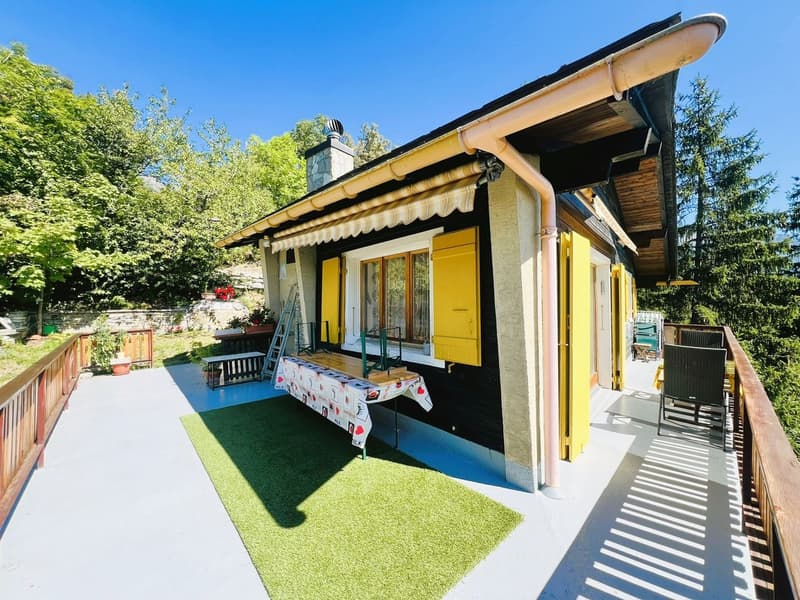 small house, yellow shutters, wooden balcony, table, chairs, green grass, trees