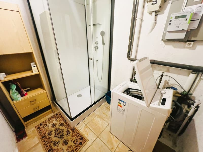 A small bathroom with a shower, a wooden cabinet, and a washing machine.