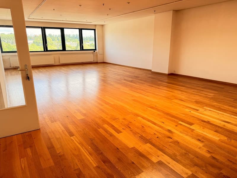Large open room with hardwood flooring, white walls, and multiple windows providing natural light. The space appears to be suitable for an office or commercial use.