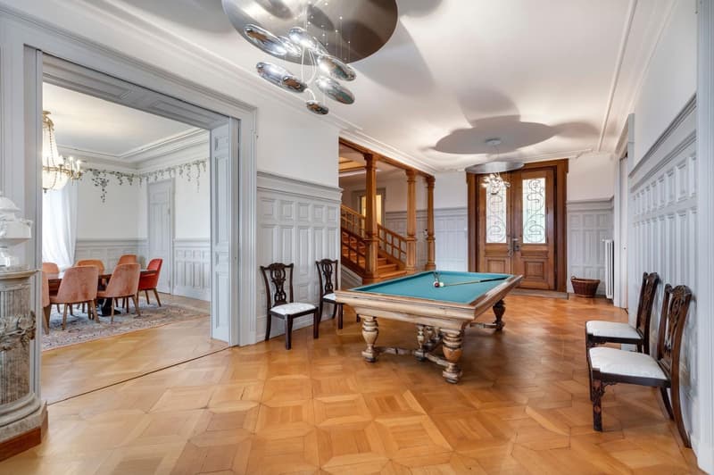 wooden flooring, wooden pool table, 2 wooden chairs on either side, chandelier, dining table and chairs, wooden staircase