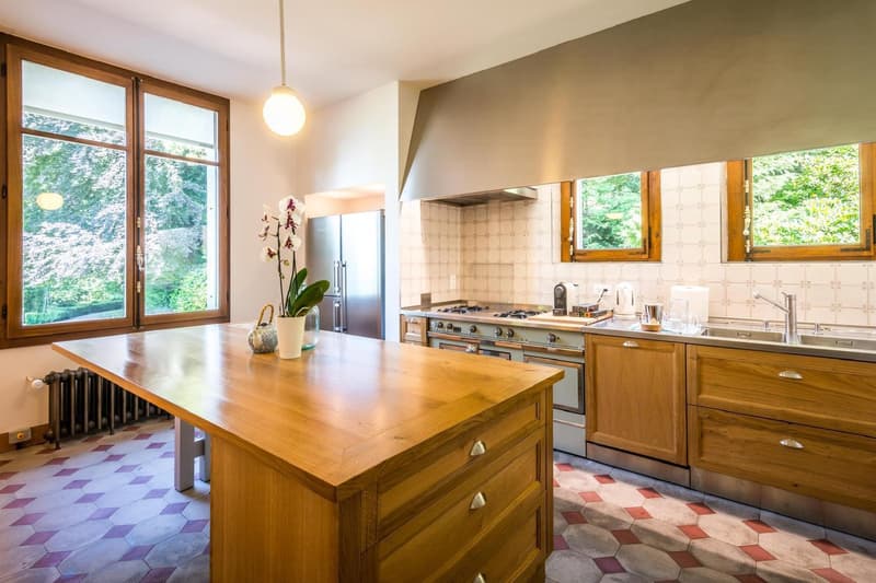 large wooden island countertop, stainless steel fridge, oven and stove, wooden cabinets, double kitchen sink, radiator