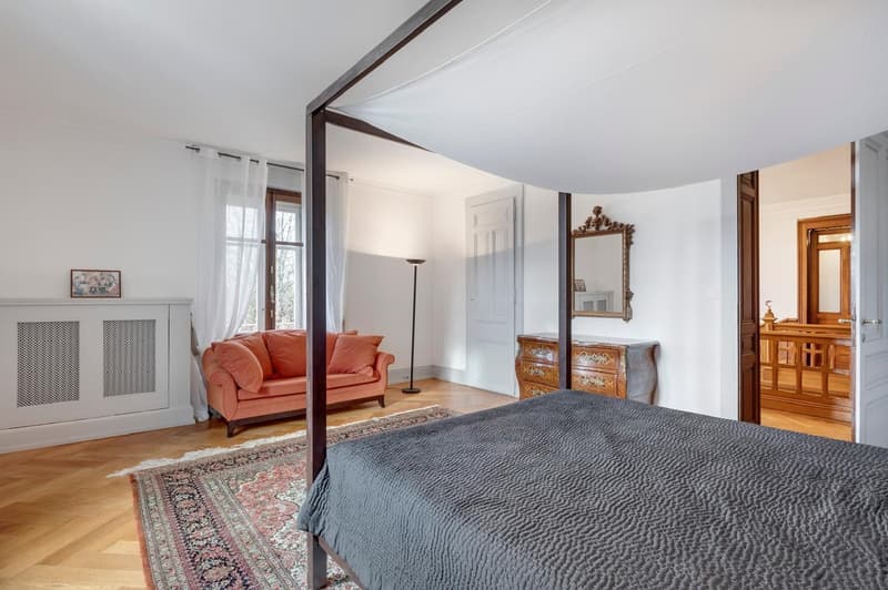 a bedroom with a four-poster bed, a rug, an orange sofa, a lamp, a mirror, a wooden cabinet, and a heater