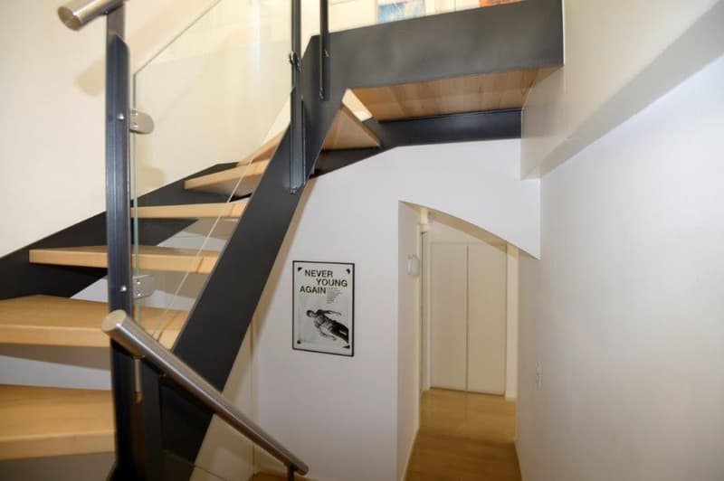 Modern wooden staircase with glass railings and black handrail