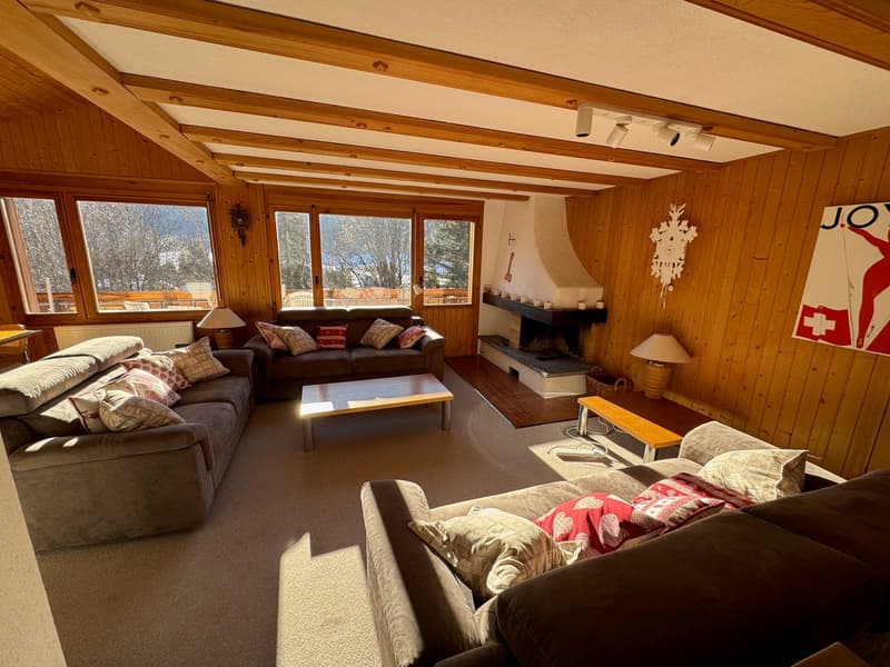 Wood paneled walls, three sofas, wooden coffee table, large fireplace, radiators, large windows, lamp, painting