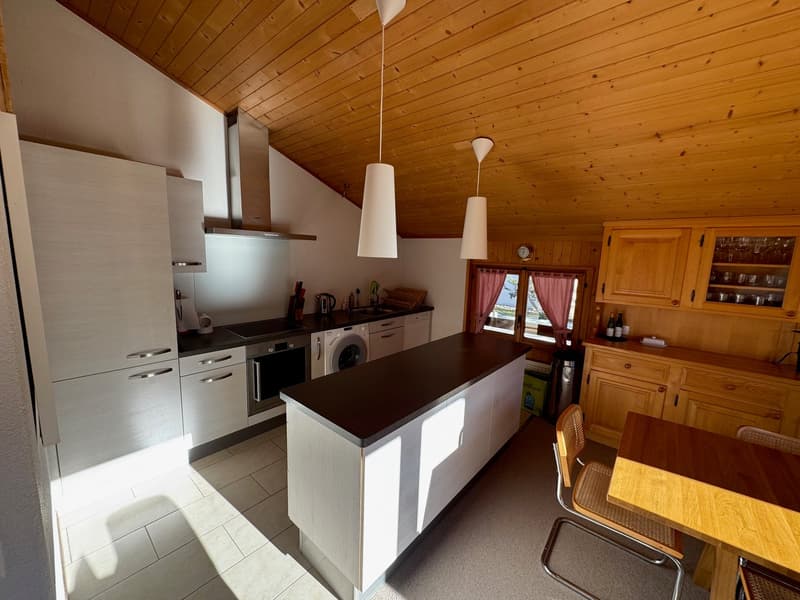 Modern kitchen with white cabinets, black counter, white fridge, washing machine, gas stove, kitchen sink, wooden table, and chairs
