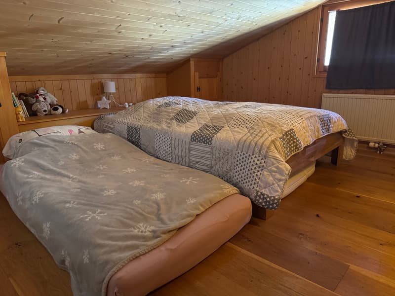 two beds with covers, wooden wall paneling, wooden ceiling, wooden floor, two lamps, radiator, window with curtain