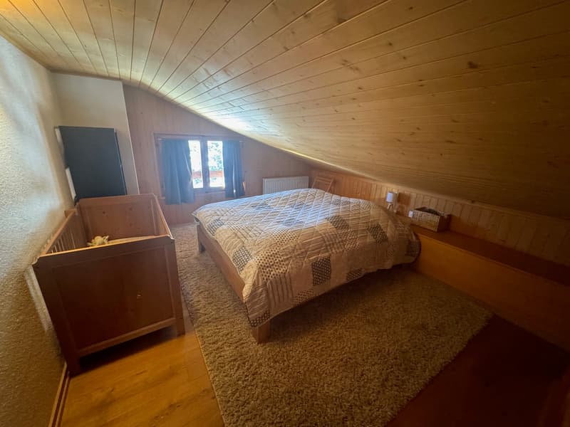 wooden bed, rug, baby crib, window with blue curtains, wooden paneling, ceiling lamp, side table with lamp, basket on shelf