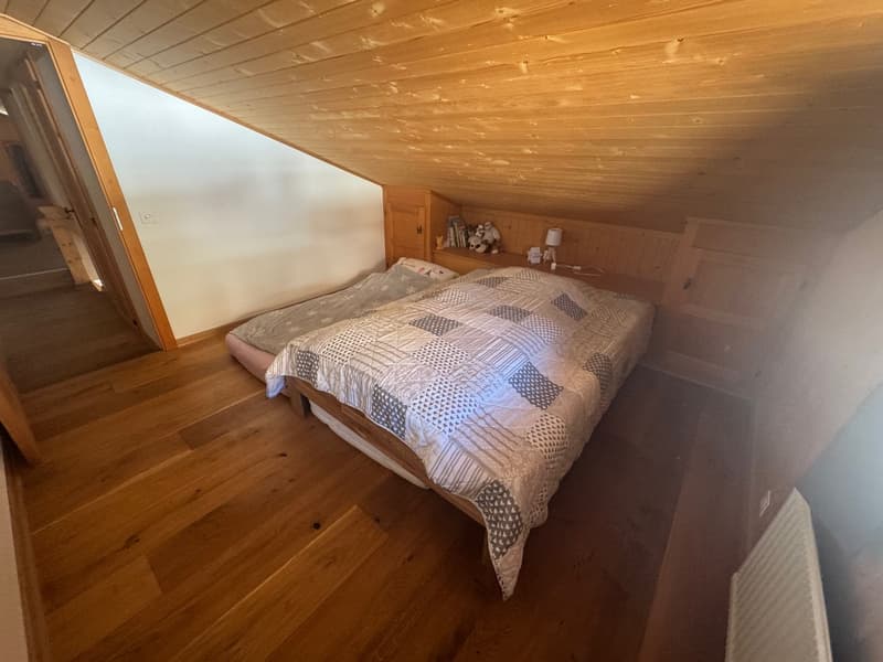 wooden ceiling, wooden bed with quilt, small table with lamp, wooden furniture, heater on wall