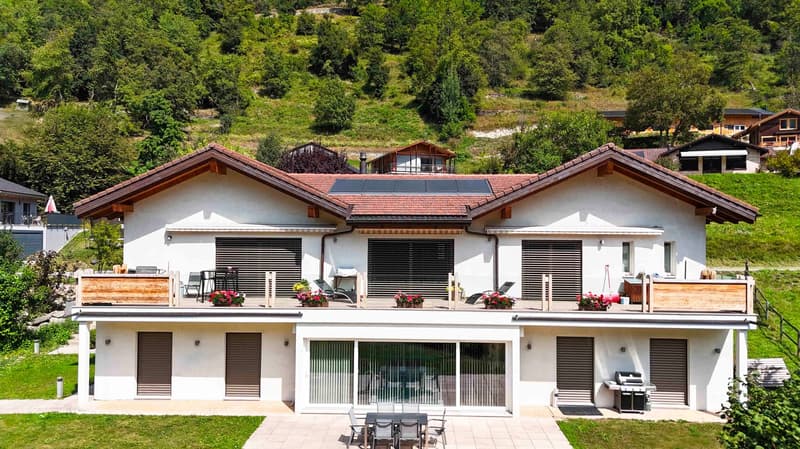 2 story white house, brown roof, solar panels, balcony with plants, outdoor BBQ, outdoor dining table, grill, green lawn