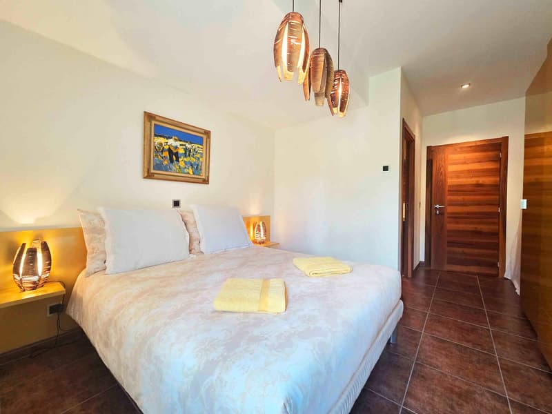 A bed with white bedding and four white pillows, a night lamp, a picture frame, and a rug are on the floor