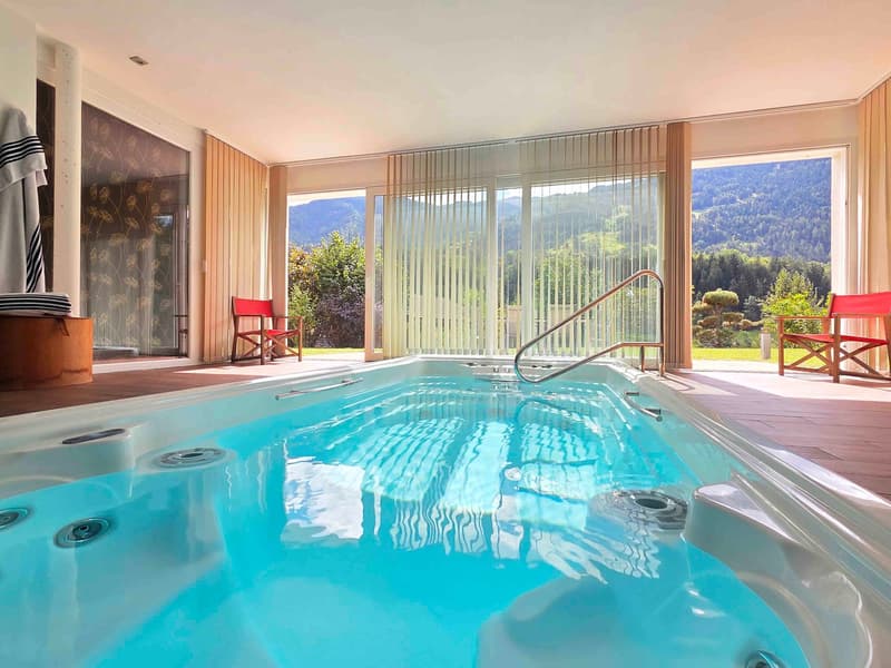 large outdoor pool, surrounded by glass walls, red chairs, mountain view