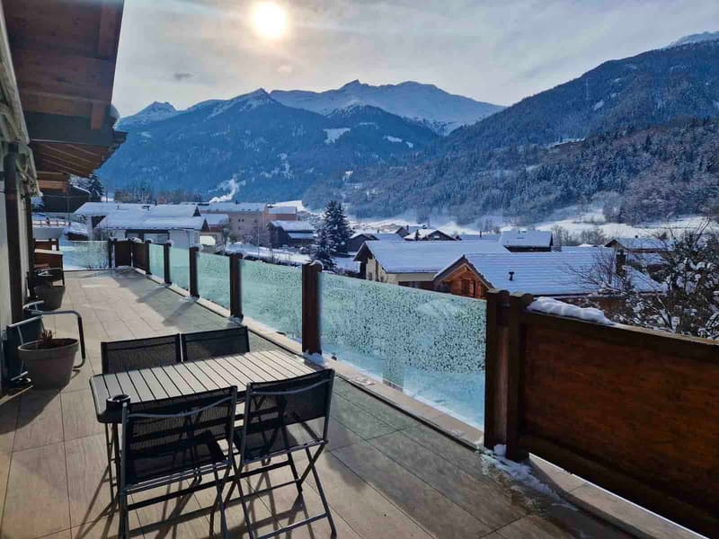 Balcony with wooden table and chairs, glass fence, scenic mountain view, wooden flooring