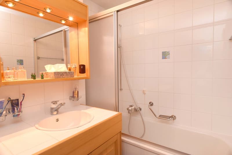 Modern bathroom with white tiles, sink, mirror, shower, and bathtub