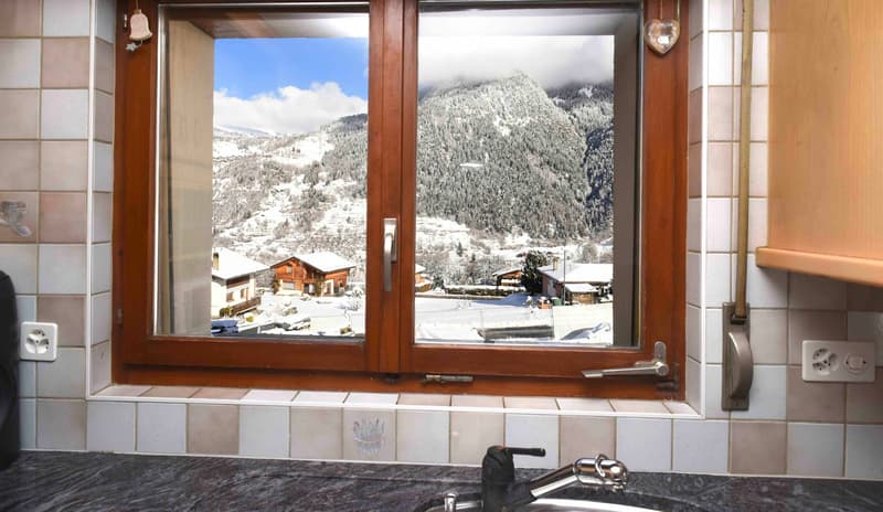 Kitchen with tiled walls, a large window with a view of the snowy mountains and houses.