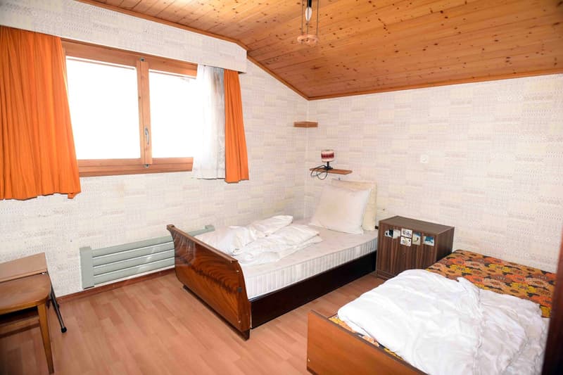 bedroom with two beds, wooden furniture, large window, white walls, wooden floor