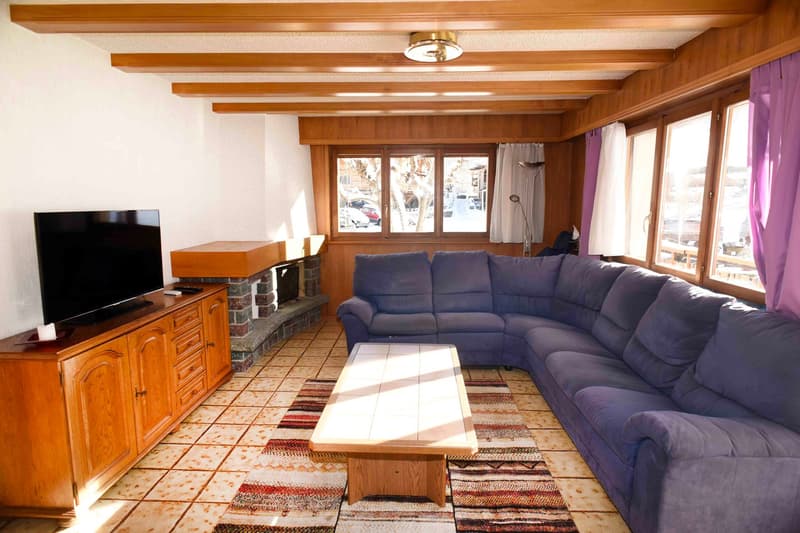 A fireplace in the corner, a couch along the wall, a TV, and large windows with a view outside