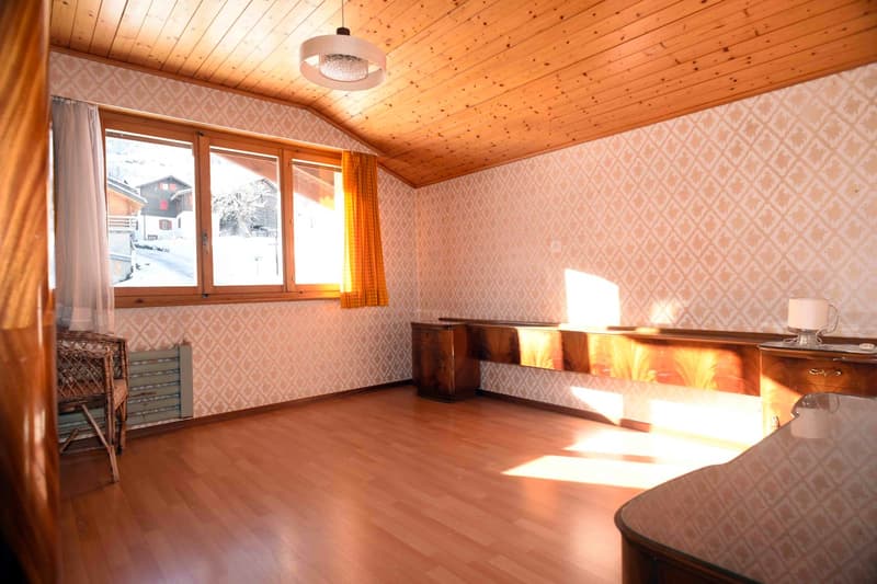 empty room with large windows, wooden floors, wooden wall panels, desk, lamp, radiator