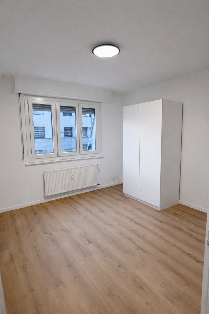 Empty room with wooden floors, large white wardrobe, white windows, white radiators, and an attached ceiling lamp