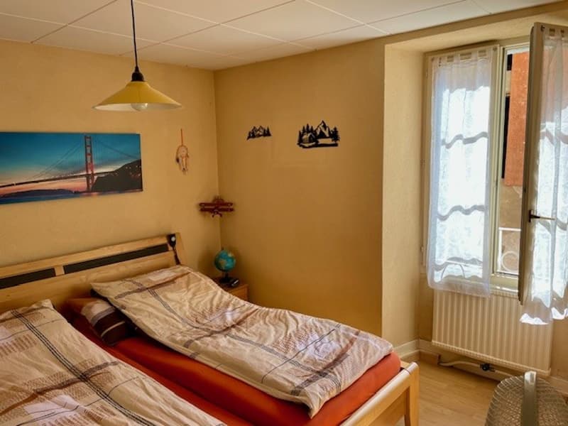 Bedroom with two beds, lamp, wall painting, window with curtains, wooden floor, radiator