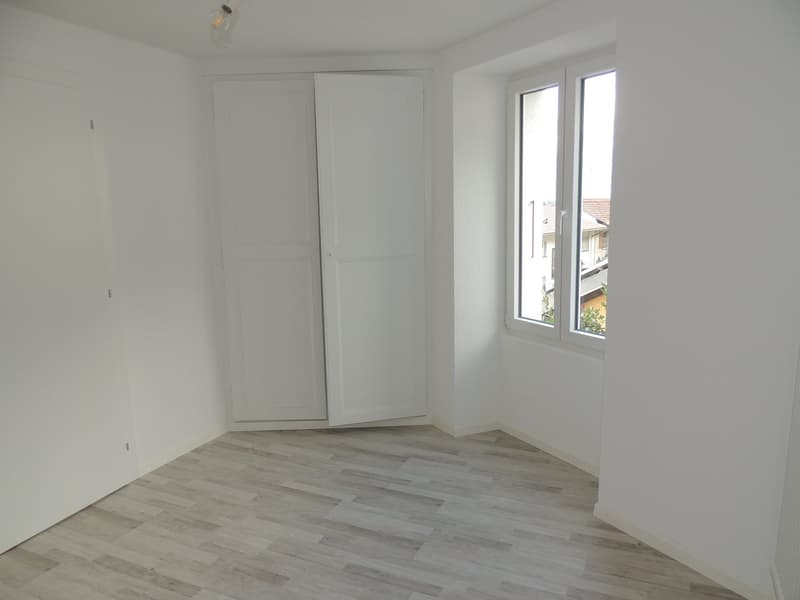 Empty room, white walls, wooden floor, large windows, two white doors
