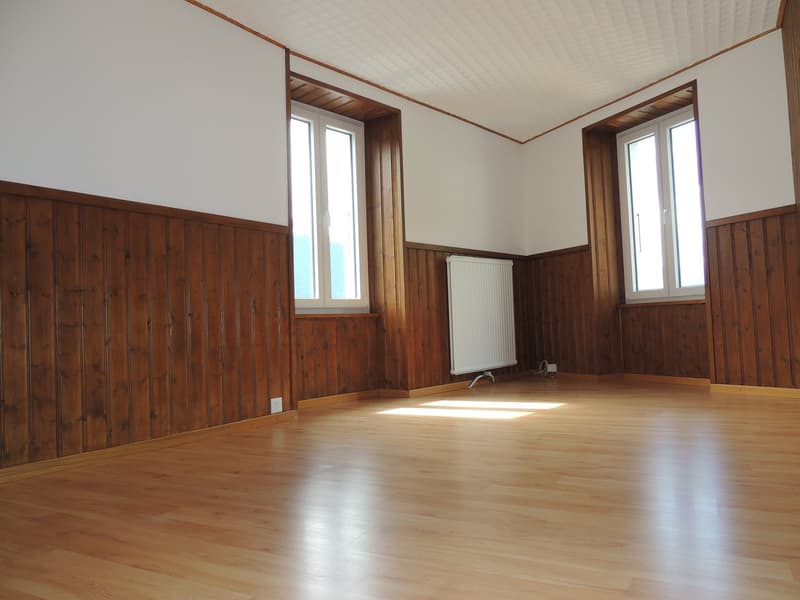 large room, wooden wall, radiator, two windows, hardwood floor