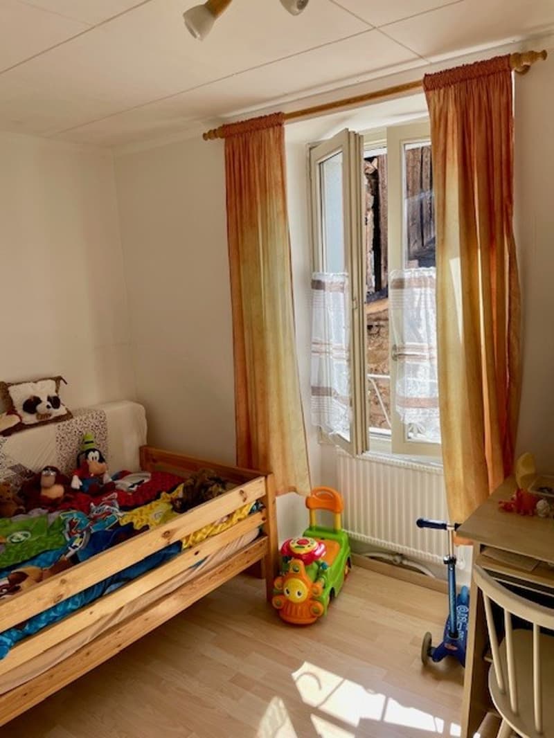 bedroom with bed, toys, table, chair, radiator, curtains, and a window