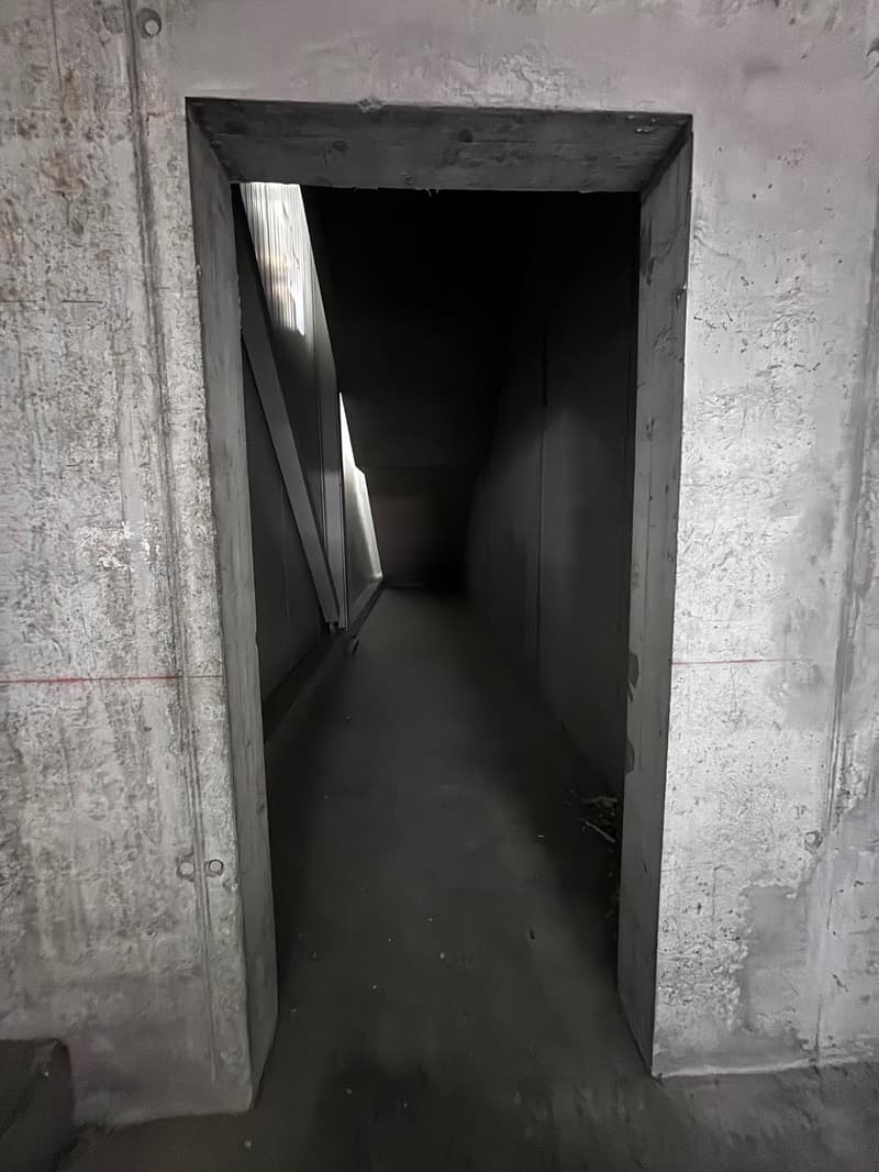 Concrete walls, a raised ground floor, a passageway leading to an underground space, and windows providing natural light.
