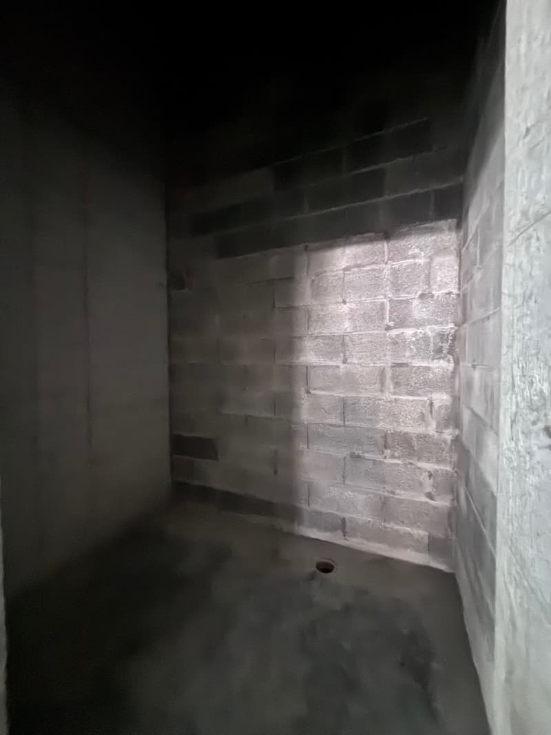 An empty room with a brick wall and concrete floor. A hole in the floor is visible.