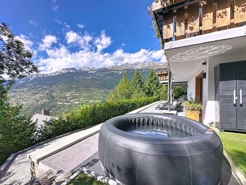 An outdoor area with a hot tub, a wooden fence, a grassy lawn, and a stunning view of the mountains.